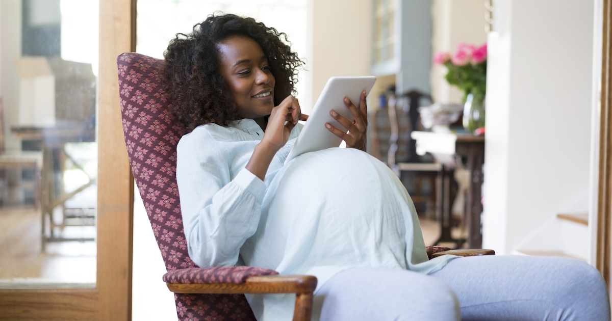 Person sitting in a chair while pregnant, looking at a tablet