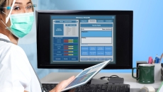 Healthcare professional standing in front of a computer with an EHR on the screen