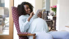 Person sitting in a chair while pregnant, looking at a tablet
