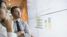 Two people looking at a board on a wall with numbers