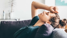 Person lying on a couch with their hand on their forehead with their eyes closed