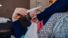 Person lying on their couch looking at a thermometer