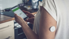 A person wearing a CGM patch is checking their blood glucose level on a mobile app