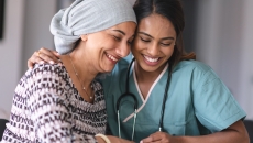 A healthcare provider with scrubs on sitting next to an oncology patient wearing a head scarf