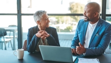 Two people sitting at a table with a laptop on it