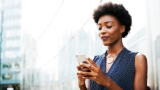 Person standing beside a building in a city looking at their phone