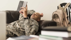 A soldier using a tablet while lying on a sofa.