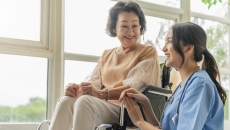 A caregiver kneeling beside a senior patient on a wheelchair