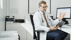A doctor using a tablet at his desk in a clinic.