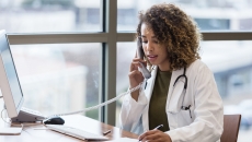 A doctor talking to a patient on a landline phone while taking notes.