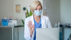 A doctor wearing a mask talking to a patient via telehealth