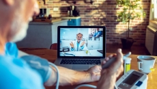A patient talking to a doctor through a video chat on his computer while using a connected blood pressure device.