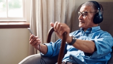An older man in his home wearing headphones and using a smartphone.