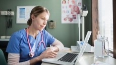 Healthcare provider in blue scrubs sitting at a desk looking at a computer