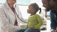 Healthcare provider and another adult standing by a child on an exam table