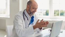 Healthcare provider sitting at a desk, wearing a lab coat and stethoscope, while looking at a computer