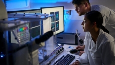 Two healthcare professionals, one sitting down and one standing up, looking at computer screens in a dark room