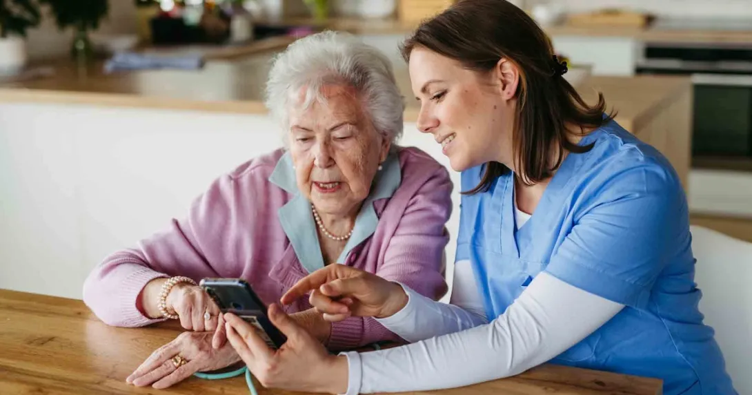 Caregiver with a patient in their home while looking at a phone