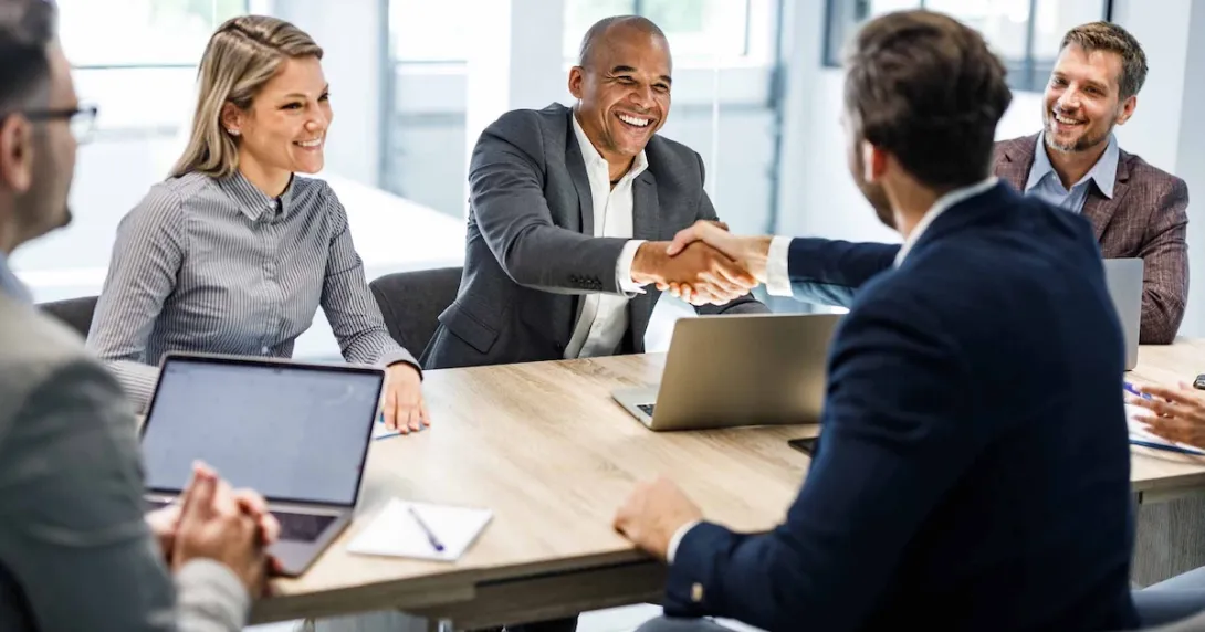 Entrepreneurs shake hands while sitting at a conference table