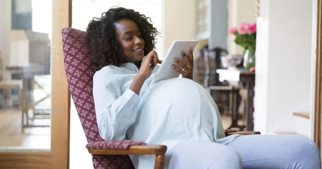 A pregnant person sitting in a chair while looking at a tablet