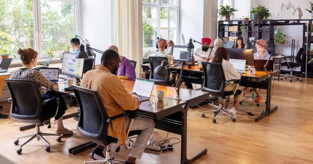 Numerous employees sitting at desks in a room with large windows