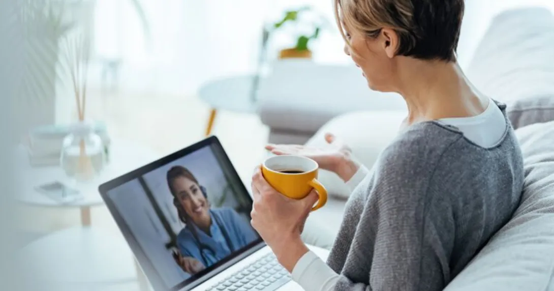 Person sitting on a couch while holding a cup and talking to a healthcare provider on their computer