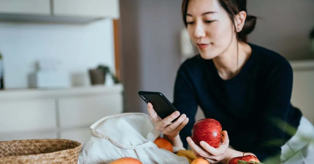 Person leaning against a counter holding an apple while looking at their phone