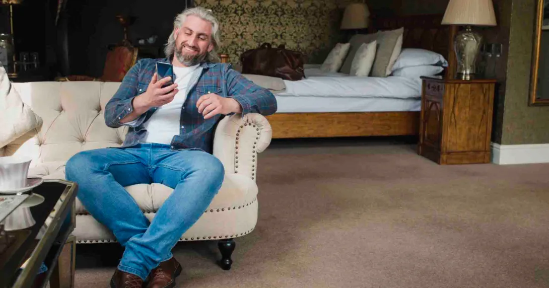 Person sitting on the couch in a hotel room smiling and looking at their phone