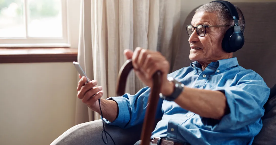 Person sitting in a chair while holding a phone and a cane and wearing headphones