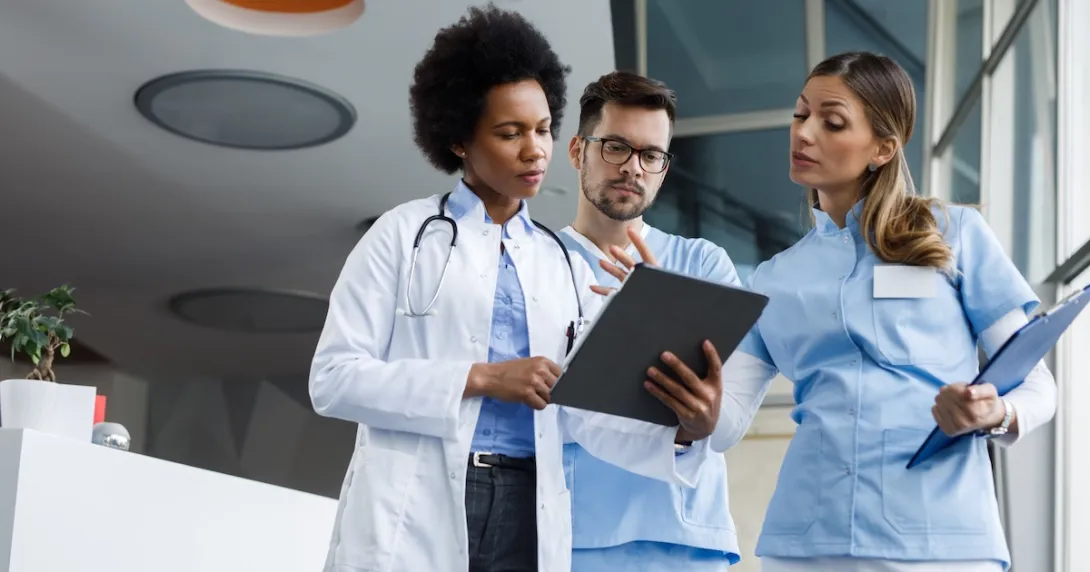 Three healthcare providers standing next to each other and looking at a tablet