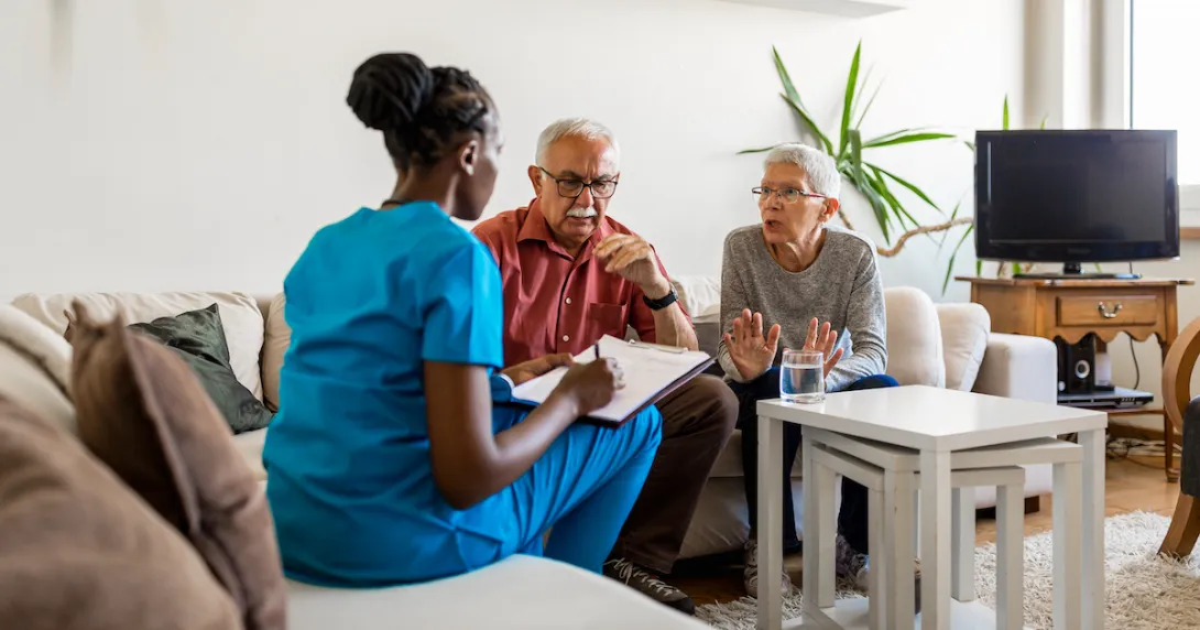 Healthcare provider in scrubs sitting on a couch in a living room with two people