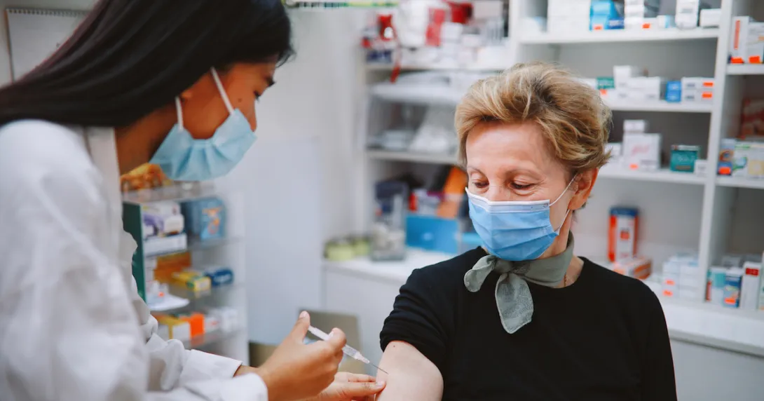 Person sitting in a pharmacy and getting an injection by a pharmacist