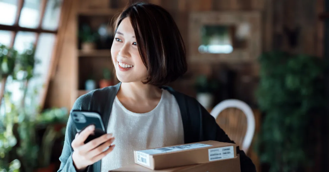 Person standing in their living room next to a lot of boxes while holding a phone