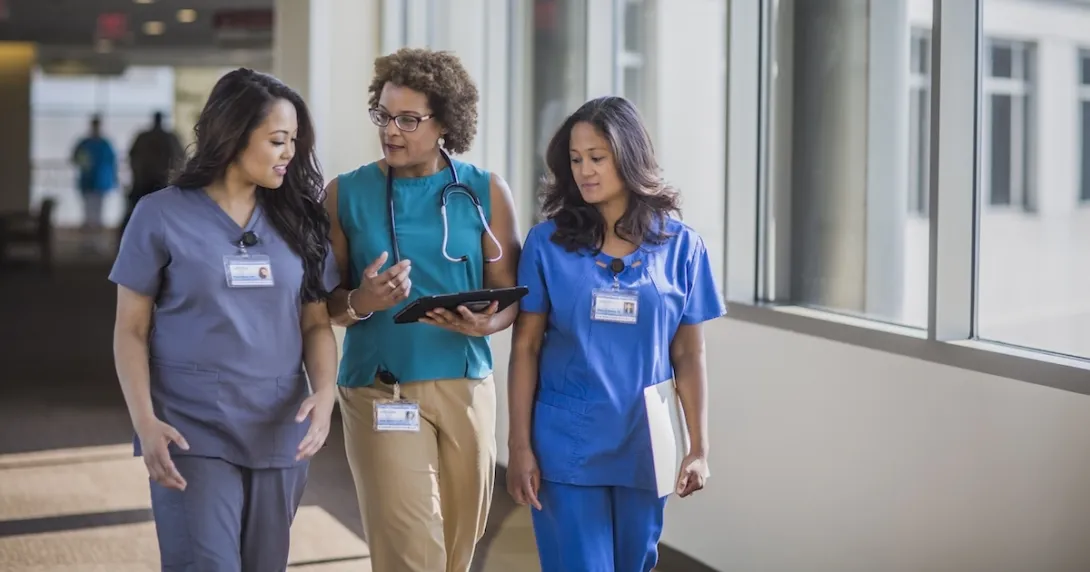Three healthcare providers walking through a hall while looking at a tablet