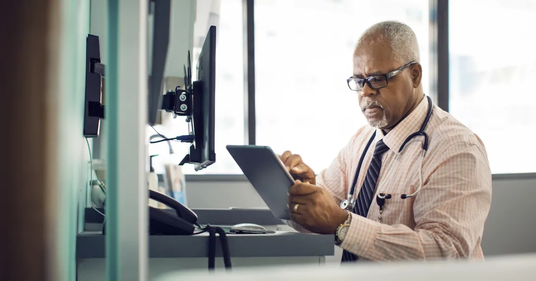Physician sitting at their desk while looking at a tablet