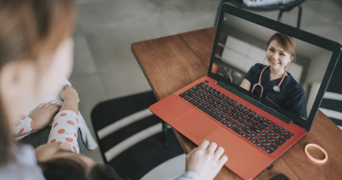 Two people sitting on a couch while looking at an orange and black computer and speaking with a virtual healthcare provider