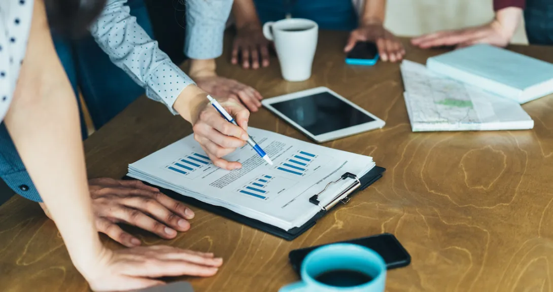 A close up of businesspeople gathered around a table looking at financial charts