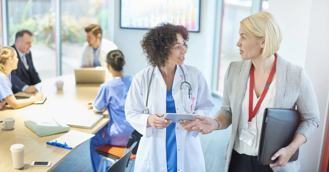 A businessperson talks with a doctor in a hospital board room.