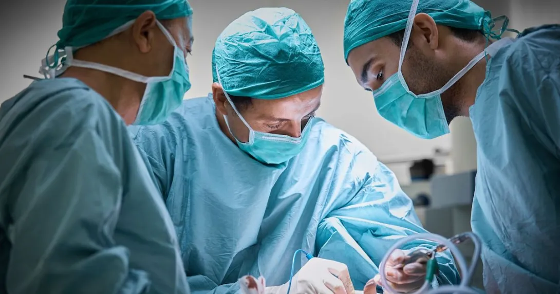 Three surgeons standing around a patient performing surgery in an operating room