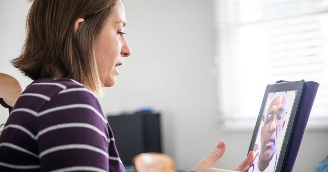 Person sitting at a computer speaking to a healthcare provider on the screen