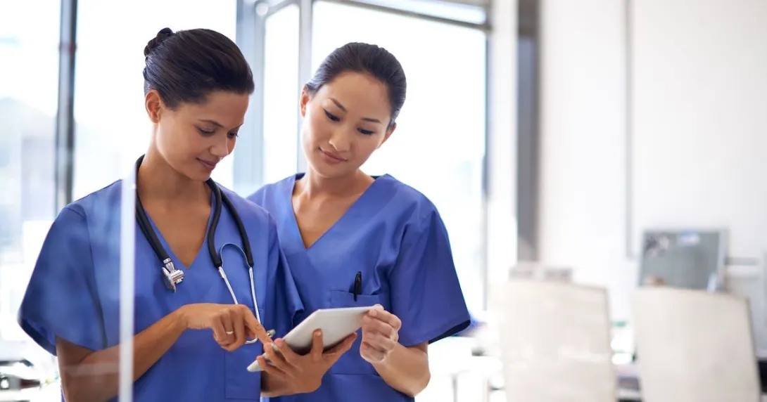 Healthcare providers standing next to each other while wearing blue scrubs and looking at a tablet