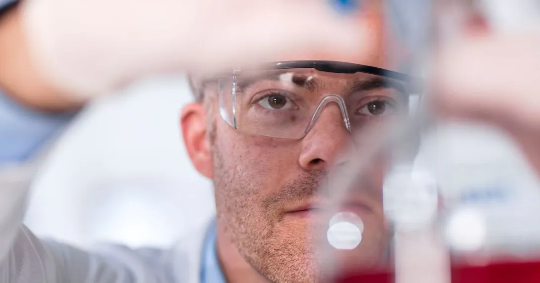 Scientist in a laboratory setting wearing safety goggles and using a beaker