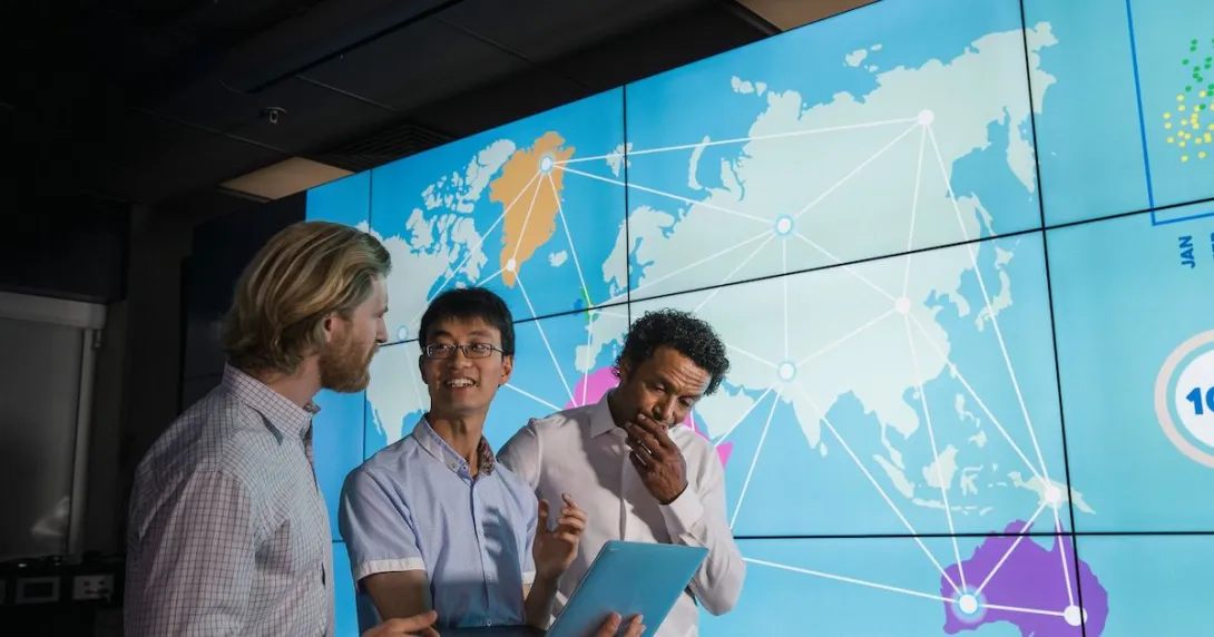 Three people standing in front of a screen showing continents connected by lines