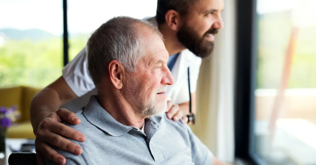 Person sitting in a chair while looking out a window with another person standing beside them