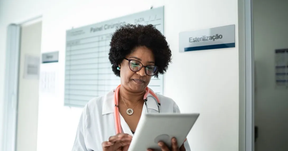Healthcare provider wearing a lab coat and a stethoscope looking at a tablet
