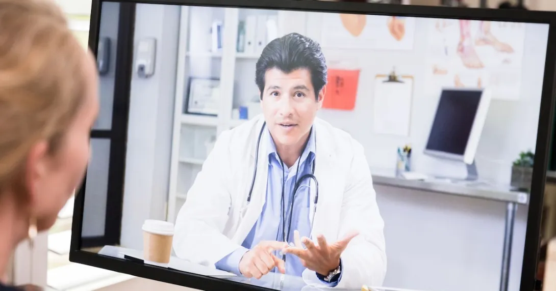 Healthcare provider on a computer screen talking to someone sitting at a desk