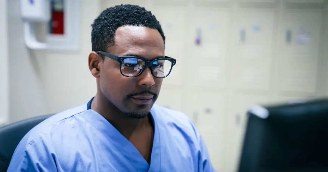 Healthcare provider wearing glasses with blue scrubs on sitting at a computer