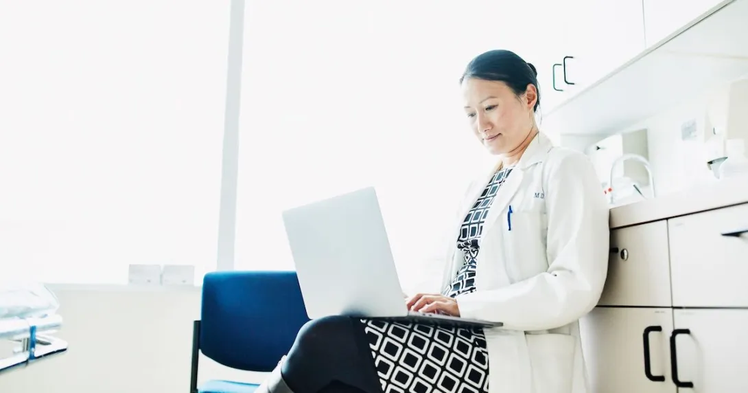 A doctor using a laptop to review a patient's file