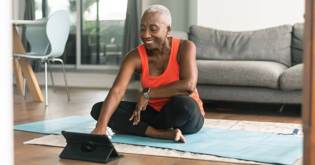 A woman sitting on a yoga mat using a tablet before she exercises