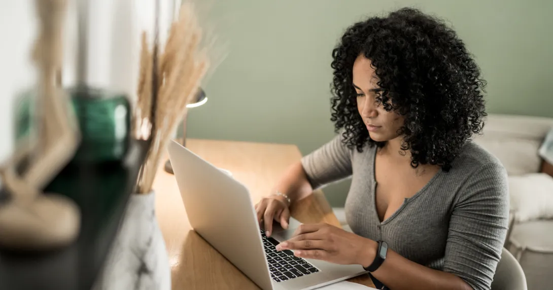 A woman using a laptop with a spreadsheet on her desk.